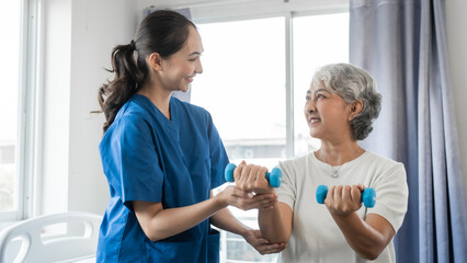 Young physiotherapist helping senior mature asian woman grey hair work out with dumbbells, to recover from injury at health centre in physical therapy session.