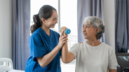 Young physiotherapist helping senior mature asian woman grey hair work out with dumbbells, to recover from injury at health centre in physical therapy session.