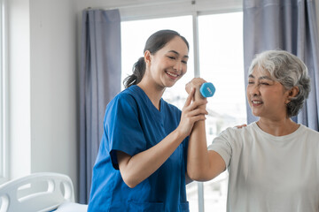 Obraz premium Young physiotherapist helping senior mature asian woman grey hair work out with dumbbells, to recover from injury at health centre in physical therapy session.