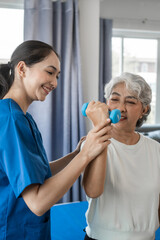 Fototapeta premium Young physiotherapist helping senior mature asian woman grey hair work out with dumbbells, to recover from injury at health centre in physical therapy session.