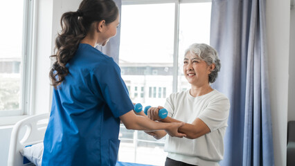 Obraz premium Young physiotherapist helping senior mature asian woman grey hair work out with dumbbells, to recover from injury at health centre in physical therapy session.