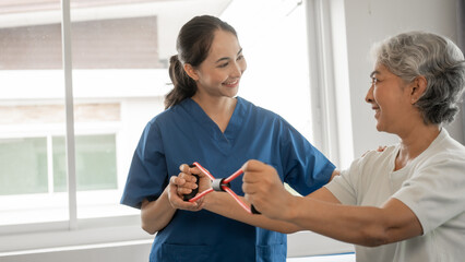 Young physical therapist caregiver assisting mature asian woman grey hair doing exercise with...