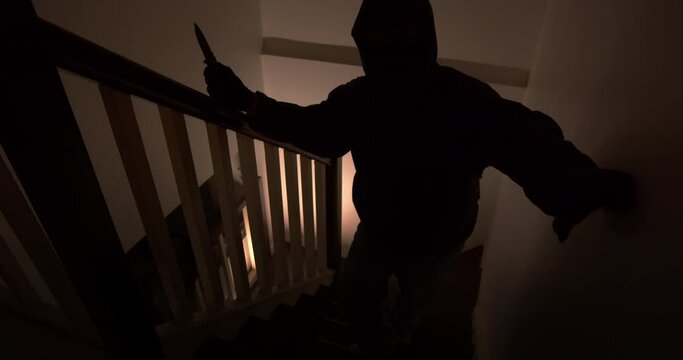 A thief with a pocket knife sneaks into the house quietly up the stairs at night.
