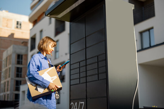 Young woman using smart phone while standing with a parcel delivered with post office machine with automatic lockers. New technologies in delivery service, self picking