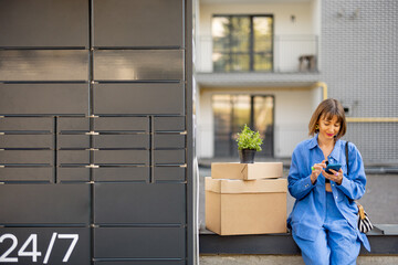 Woman sits with a cardboard packages and flowerpot near post office machine and using mobile phone at residential district. Concept of delivery or relocating