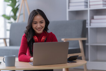 Naklejka premium Asian beautiful woman in the living room,listening to music and playing social media with mobile phone and laptop for relaxing, studying online. University student concept.