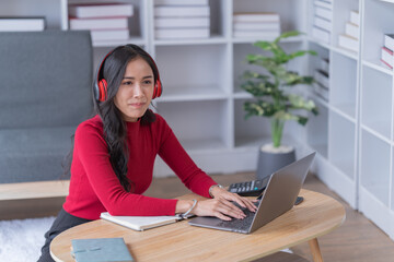 Asian beautiful woman in the living room,listening to music and playing social media with mobile phone and laptop for relaxing, studying online. University student concept.