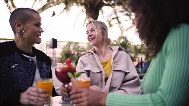 Three cheerful mature women having drinks outdoors in a terrace, toasting with cocktails or mocktails. Female friends having fun together gathering in a bar.