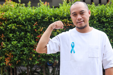 Smiling Asian young man with blue ribbon show power strength beat disease. Prostate cancer awareness concept. 