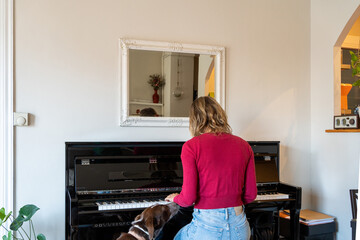 unrecognisable woman with unrecognisable back playing piano with a dog looking at her, practising...