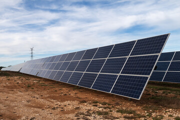 Vista de un huerto solar con sus placas solares y una torre eléctrica al fondo.