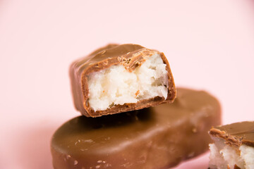 Sweet chocolate bar with coconut flakes macro on pink paper background with copy space