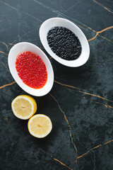 White bowls with red and black caviar on a dark-olive marble background, vertical shot with copy space, above view