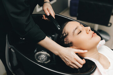 The hairdresser washes the head of a girl in a barbershop. brunette came for a haircut