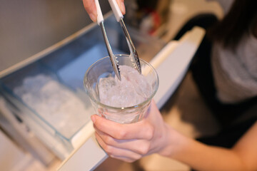 冷蔵庫から氷を取り出してコップに入れる女性の手元のクローズアップ