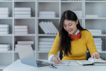 Young adult happy smiling, Asian student wearing headphones talking on online chat using laptop in university College female student learning remotely.