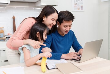 Obraz premium Beautiful asian women Lovely girl Looking at the laptop screen Of handsome men working online on the desk at home It's a new normal life for the family.