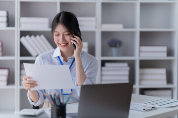 Portrait of young professional businesswoman writing on paper and use smartphone while sitting at office.