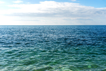 Blue sea water surface and horizon, blue sky and light clouds. Light ripples, waves on the sea.