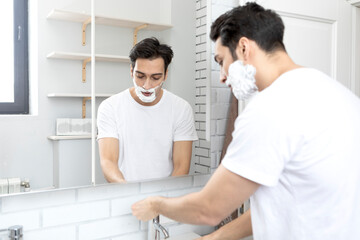 Fototapeta premium Handsome man looking at the mirror and shaving in the bathroom 