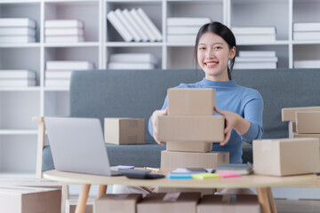 Asian business woman siting on sofa using a laptop and notebook checking order online shipping boxes at home. Starting SME Small business entrepreneur freelance. Online business, SME Work