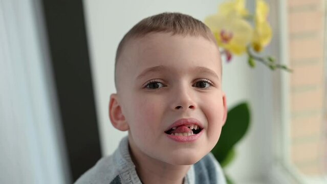 A brave little boy of 7 years old shakes his baby tooth. Change of teeth in children. Self-treatment at home.