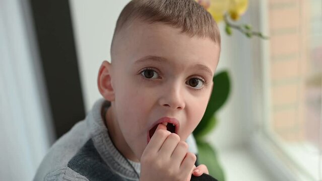A brave little boy of 7 years old shakes his baby tooth. Change of teeth in children. Self-treatment at home.