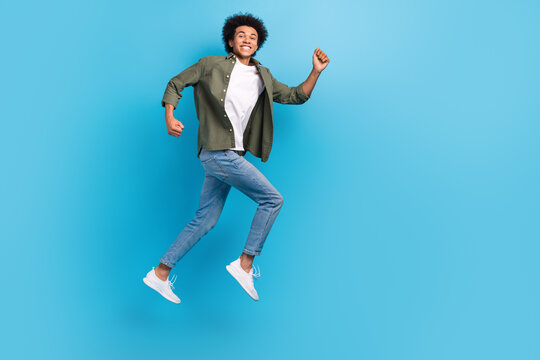 Full body photo of active young guy running wear khaki shirt denim jeans fast speed jumping positive isolated on blue color background