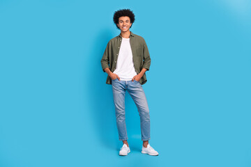 Full size portrait of satisfied glad young person put arms pockets posing isolated on blue color background