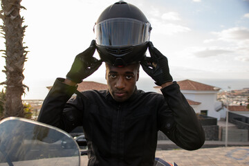 Close up of an African American biker getting ready to ride wearing his helmet. Road safety concept.