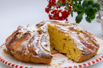 Apple pie sprinkled with icing sugar on plate with red flower in background