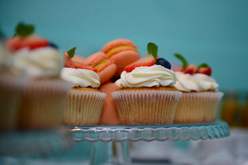 Delicious vanilla cupcakes with cream cheese, decorated with pieces of fresh strawberries and blueberries on a plate, in selective focus. Muffins with white cream and strawberries. Birthday dessert