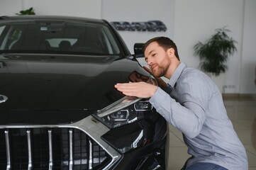 Fototapeta na wymiar Visiting car dealership. Handsome bearded man is stroking his new car and smiling