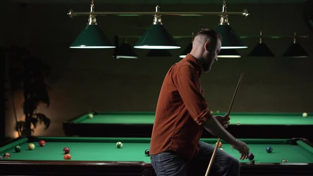 Caucasian man preparing his billiards cue sitting on pool table.