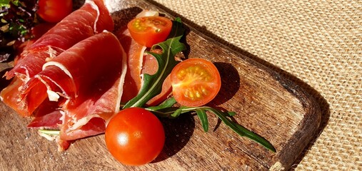 Jamon sliced ​​on a wooden board with tomatoes and herbs. Spanish jamon on the board....