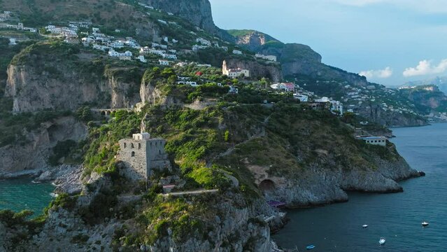 Aerial drone view passing by a Stone Tower on a rocky Coast with blue Sea view. Torre Capo di Conca - a historical landmark on Conca dei Marini, Amalfi COast, Italy, Europe.