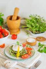 Poached egg opens with yolk leaking on zucchini and greens fritters on a plate of pea microgreens and tomatoes. Blurred background