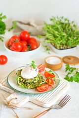 Poached egg on zucchini and greens fritters on a plate with pea microgreens and tomatoes. Blurred background