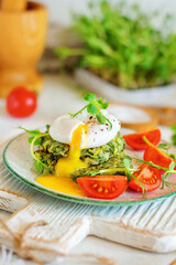 Poached egg opens with yolk leaking on zucchini and greens fritters on a plate of pea microgreens and tomatoes - close-up. Blurred background and foreground