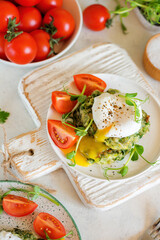 Poached egg with leaking yolk on zucchini and greens pancakes on a plate with pea microgreens and tomatoes on a served table.