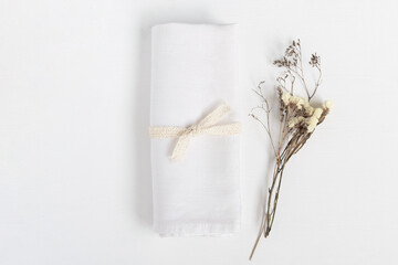 Linen napkin tied with ribbon on white table. Fabric and dried flowers in rustic style for mock up.