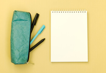 Top view of a Desk with a pencil case and an empty Notepad on a yellow background. Flat lay of items with space for text.