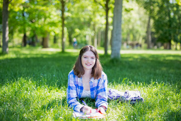 Front view of a student girl studying reading notes outdoors sitting on the grass in a park