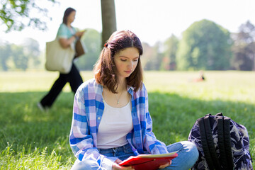 Front view of a student girl studying reading notes outdoors sitting on the grass in a park