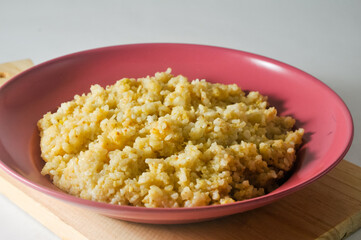 Fried rice, an Indonesian specialty, is served on a red plastic plate on a wooden board isolated on a white background