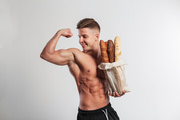 Handsome happy muscular athlete fit man with a healthy muscular body holds bread baguettes in a...