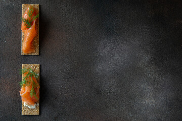 Crisp bread with cottage cheese and salted salmon on dark brown background