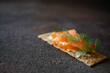 Crisp bread with cottage cheese and salted salmon on dark brown background