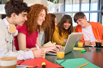 Group of cheerful Caucasian students gathered in university cafeteria to work and discuss project topic together. Smiling responsible young people using laptops to prepare homework. Generation z.