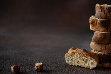 Italian biscotti with hazelnuts on wooden plate on dark brown blurred background 